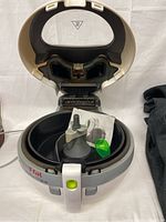 Open top view of T-fal ActiFry fryer showing the inner removable stirring paddle, green plastic spoon, and instruction booklet inside the cooking pan.