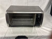 Front-facing photo of Black & Decker stainless steel toaster oven with glass door open showing interior wire rack and control knobs.