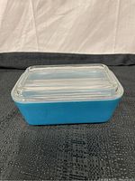 Rectangular blue Pyrex refrigerator dish with smooth clear glass lid placed on top, showing exterior and lid design.