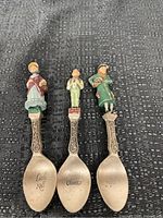 Top-down photo showing all three pewter spoons with painted figurines and engraved character names on each bowl: Little Nell, Oliver, and Fagin.