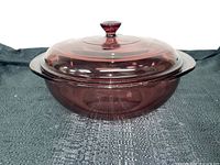 Photo showing angled view of cranberry glass covered casserole dish with knobbed lid on textured black background