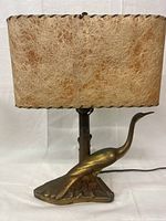 Full side view of vintage brass peacock lamp with light brown fibrous rectangular shade showing elongated peacock body and neck as base.