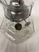 Close-up of the Lamplight Farms gold seal on the glass base showing brand authenticity.