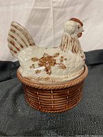 Front angle view of the white ceramic hen with brown floral accents on a basket base.