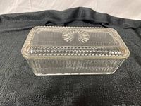 Side view of the clear glass rectangular container with lid on a dark textured cloth, showing starburst pattern on lid and vertical ridges on sides.