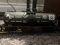Side view of black tanker car model train labeled PCx with technical markings and serial number.