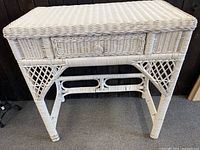 Photo showing the front view of the white wicker desk featuring a single drawer and woven wicker legs.