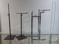 Photo showing all four metal retail display stands with different styles and bases on a glass surface against a white wall.