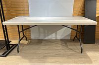 Front view of Lifetime plastic folding table with metal folding legs on wood floor and light background