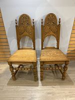 Pair of antique solid oak chairs front view showing carved wooden seats, turned legs, stretchers and tall arched carved backs with finials.