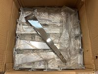 Box containing 14 new metal grid wall shelf brackets sealed in plastic bags, stacked neatly inside a cardboard box.