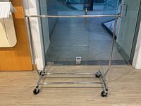 Front view of the chrome-plated extendable clothing rack showing horizontal hanging bar and caster wheels.