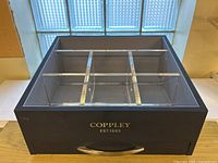 Navy blue unbranded rectangular display box with acrylic dividers on top dividing it into six sections and a front drawer.