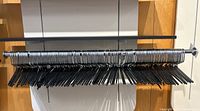 Full view of over 130 metal pants hangers arranged on a horizontal rod, showing the coated lower bars.