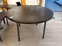 Full view of large round oak table with steel legs on a laminate floor, showing the top and legs.