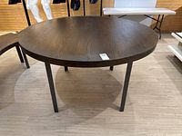 Front angle view of a large round oak veneer table with steel legs on a wooden floor.