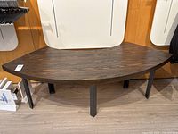 Front view of a semi-circular oak veneer table or bench showing wood grain top and black steel legs on light wood floor