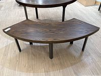 Photo of curved oak veneer table or bench on wood-like floor. Shows wood grain detail, curved shape, and steel legs.