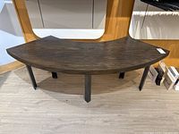 Front view of the oak veneer curved table or bench with steel legs on light wood floor, showing curved top and sturdy steel legs.