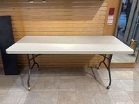 Front view of the off-white plastic rectangular tabletop with black folding metal legs, showing overall good condition and size.