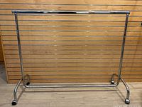 Full front view of the modern rolling clothing rack showing the tubular chrome metal frame with horizontal bars and castor wheels.