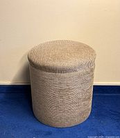 Front view of the round fabric stool, showing the textured beige upholstery and rounded cushion top.