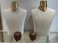 Photo showing two identical fabric covered torso mannequins with gold neck pieces and brown faux wood bases placed side by side on a glass surface.