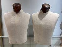 Two fabric covered torso mannequins with removable dark wooden neck pieces displayed side by side on a glass shelf