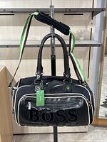 Front view of the black Hugo Boss gym bag showing large raised BOSS logo and green/white striped shoulder strap with tag attached.