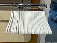 Front view of 31 white wooden hangers lined up on a metal rod, showing the uniformity and quantity.