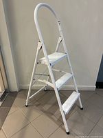 Three-step white folding metal step ladder standing upright showing full front and angled views.