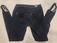 Back view of the black jeans showing embroidered butterfly and apple designs on the back pockets and stirrup straps on the hems.