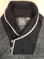 Close-up of the black cowl neck with light gray trim and two black buttons, showing waffle knit texture and collar details.