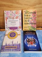 Front cover of four aromatherapy books laid out on wood surface, colorful and botanical designs.