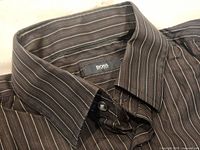 Close up of collar and logo label inside the shirt showing 'BOSS Hugo Boss'. Dark brown fabric with thin vertical stripes.