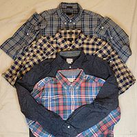Four men's J Crew cotton shirts laid out folded and stacked, showing various plaid and patterned designs.