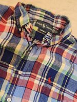 Close-up of the Ralph Lauren label, custom fit and button collar, fabric plaid pattern in multiple colors with the red embroidered pony logo.