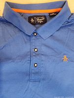 Blue Penguin by Munsingwear polo shirt laid flat showing collar, buttons, and embroidered penguin logo on chest.