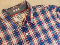 Close-up of the collar, chest pocket, brand label, and plaid pattern showing red, white, and blue colors with visible Penguin logo.