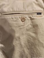 Close-up of back pocket showing button closure and Polo label tag on light tan cotton khaki pants.
