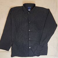 Full view of button-up black nightshirt laid flat, showing collar, buttons, chest pocket, and long sleeves