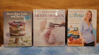 Front covers of three cookbooks showing titles and images: cake, frozen desserts, and Anna Olson
