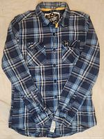 Full front view of the blue plaid long-sleeve shirt with folded arms laid flat, showing chest pockets and button details.