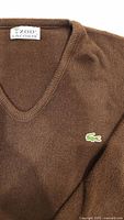 Close-up image of the brown vintage Izod Lacoste V-neck sweater neckline and embroidered green crocodile logo on the chest.