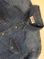 Front view of Wrangler denim shirt showing pearl snap buttons, flap pockets with snap buttons, and western yoke design.