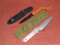 Two survival/bushcraft knives laid out with their sheaths on a red surface.