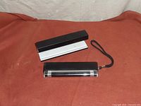 Two blacklight counterfeit detectors and a black and white stand on a reddish-brown surface.
