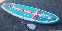 Inflated paddle board laid flat on gravel alongside one paddle section