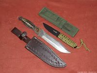 Two camping knives and their sheaths laid out on a red surface: large bone handle knife with leather sheath and smaller black blade knife with paracord handle and green fabric sheath.