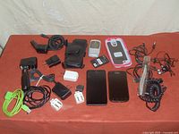 Photo of all items spread on table: 2 smartphones, flip phone, phone cases, chargers, cables, earphones, and a black pouch.